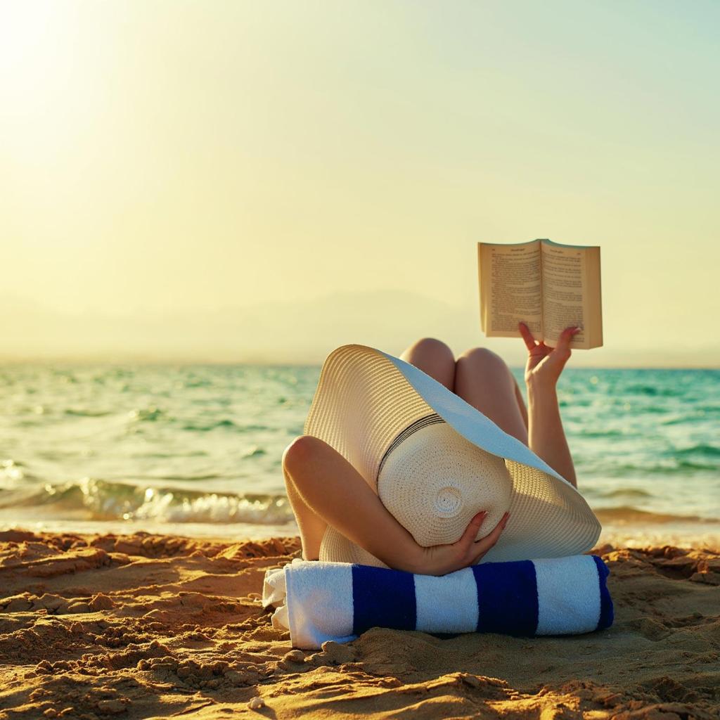 Young woman reads book beachside during sunset.
