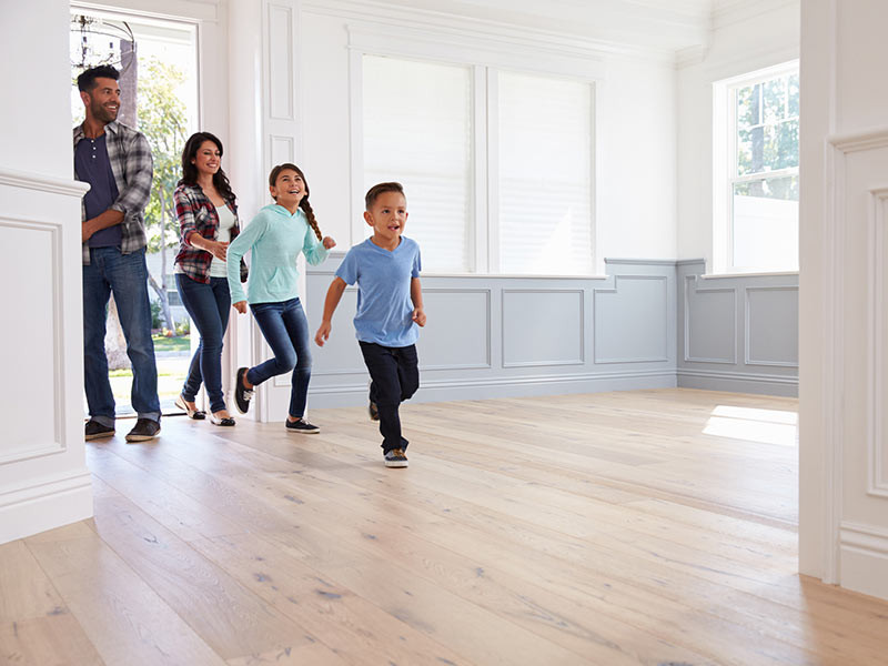 Two children excitedly entering an empty new home while their smiling parents walk through the front door behind them