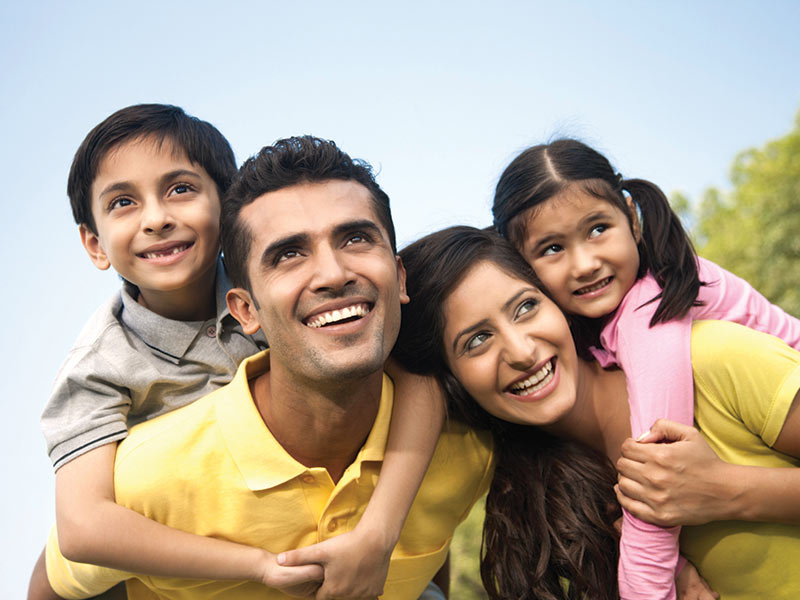 Smiling couple outside each carrying a young happy child on their backs