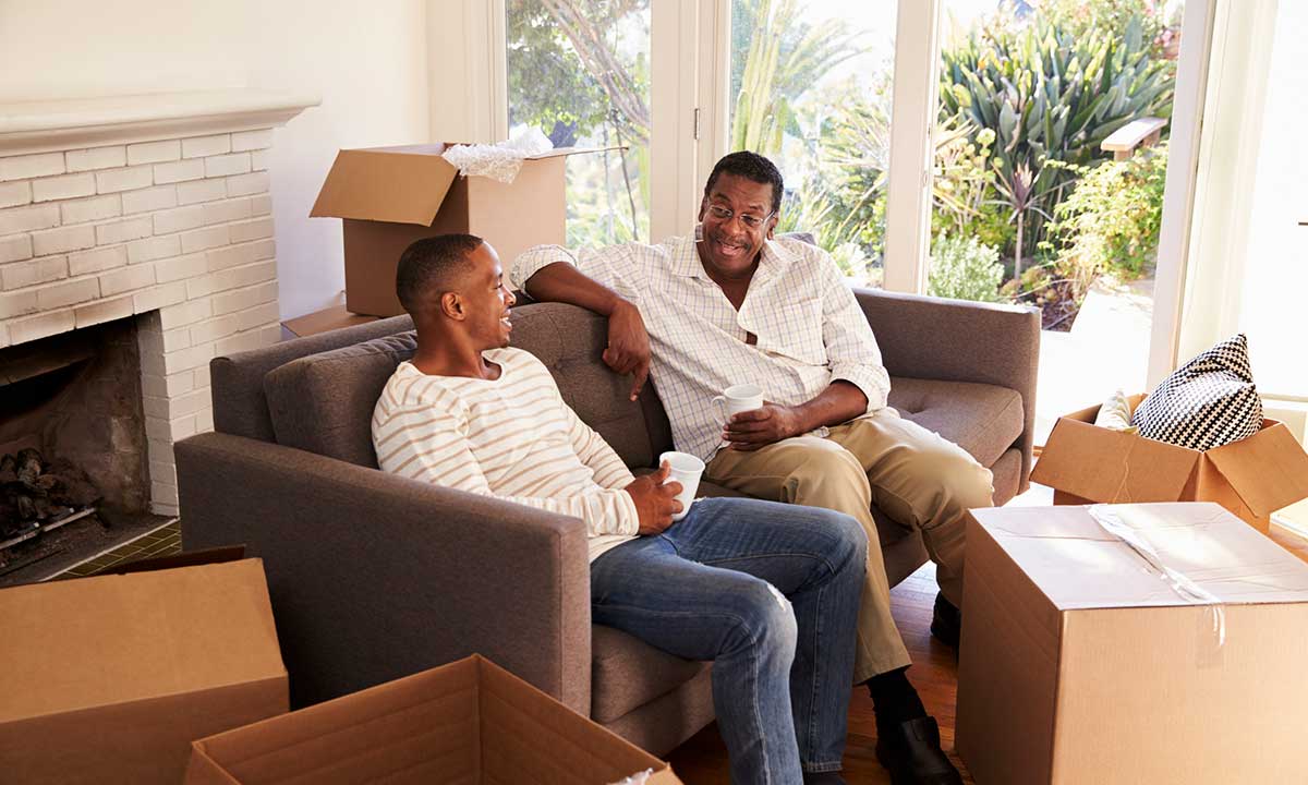 A father and son sitting on a sofa and unpacking boxes.