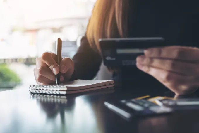 A girl writing down on notepad and using calculator.