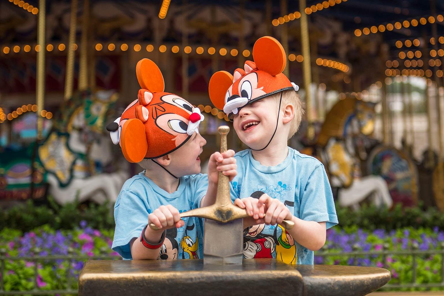 Two young brothers laugh while trying to pull out the sword in the stone at the Magic Kingdom.