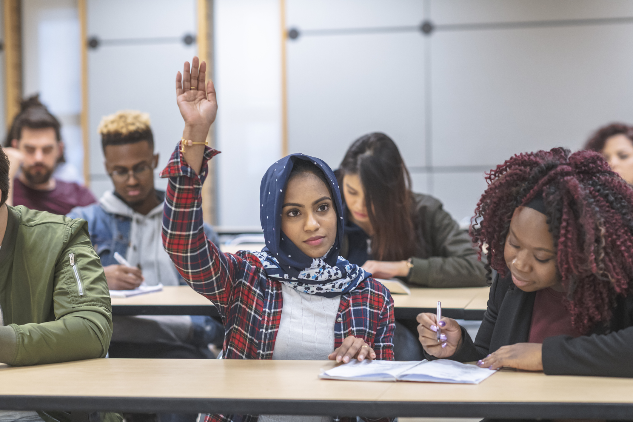 A female international student raising her hand in class, surrounded by other students