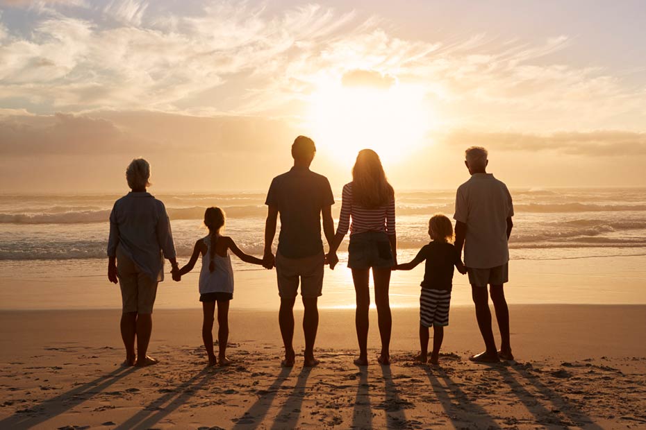 A multi-generational family holding hands on a beach