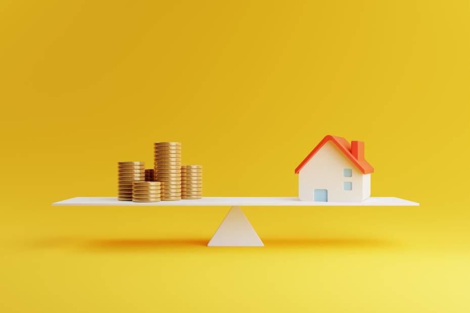 A balanced wooden seesaw with a model home on the right and stacks of loonies on the left