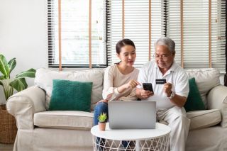 Asian woman teaching a senior to use credit card and phone for online shopping