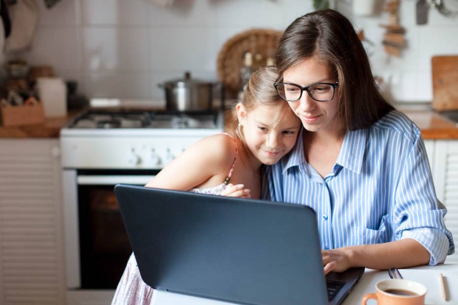 A smiling mother and daughter hugging, looking at a laptop