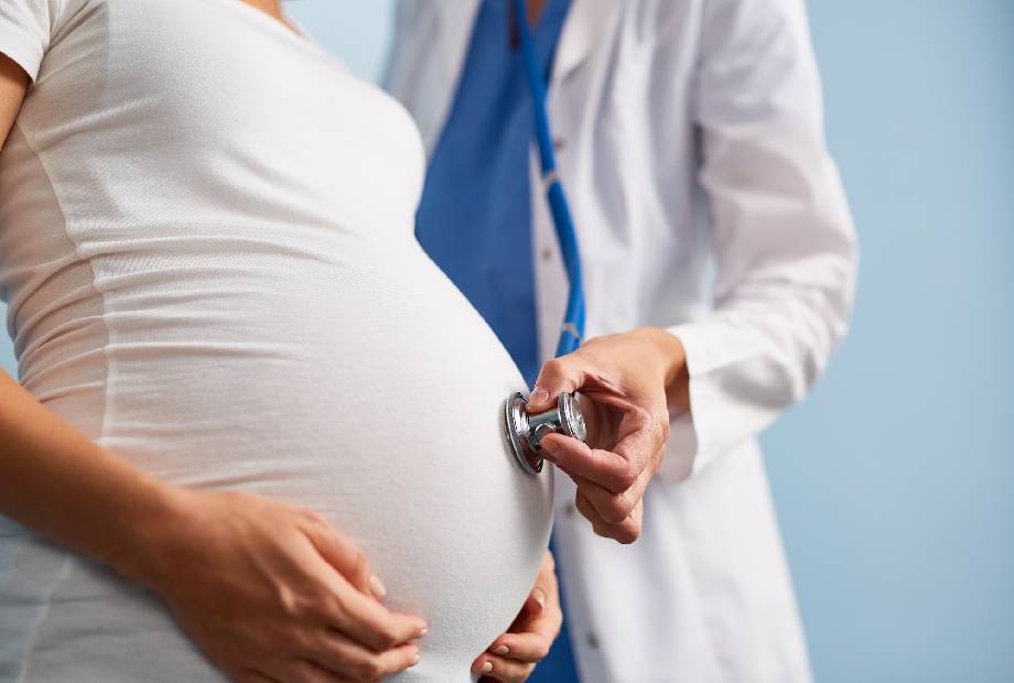A doctor listening to the baby heart rate in pregnant female abdomen
