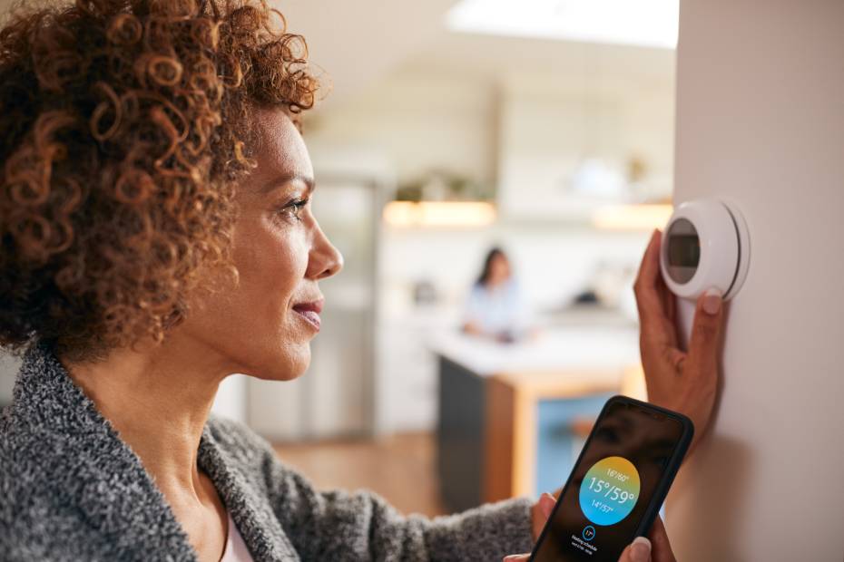 Woman using a smart thermostat to control her home's central heating