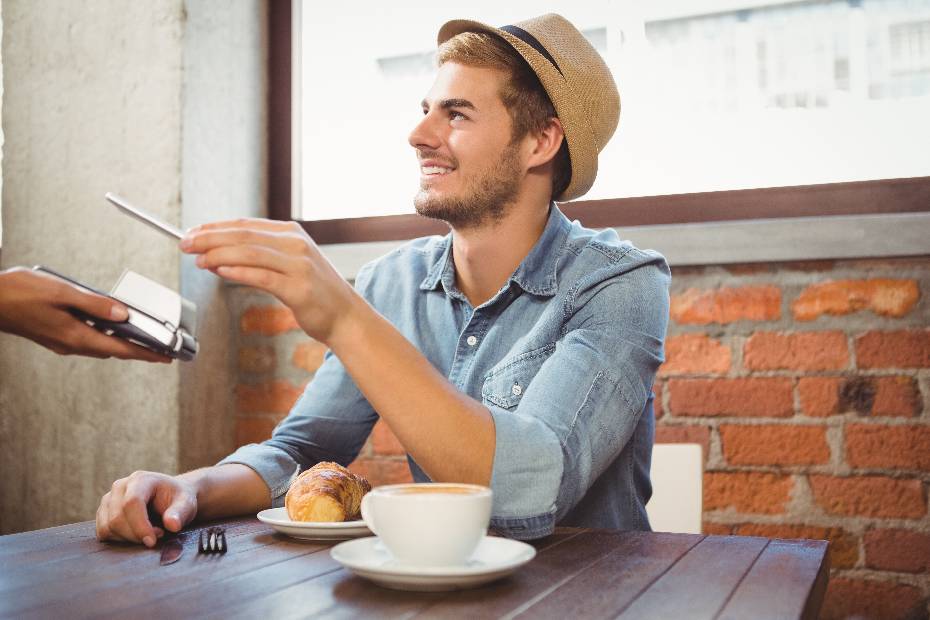 Handsome hipster student tapping to pay with his smartphone mobile device at a coffee shop