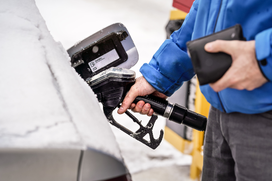 Man holding fuel nozzle, filling gas tank of diesel car covered with snow