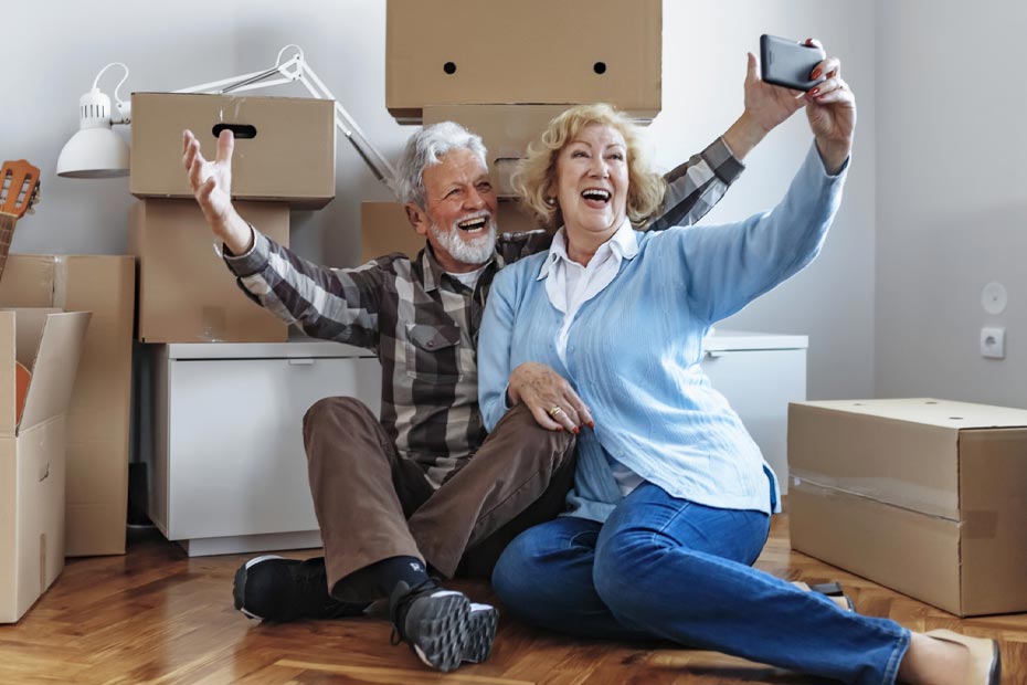 Senior couple sitting down after the move in to take a selfie.