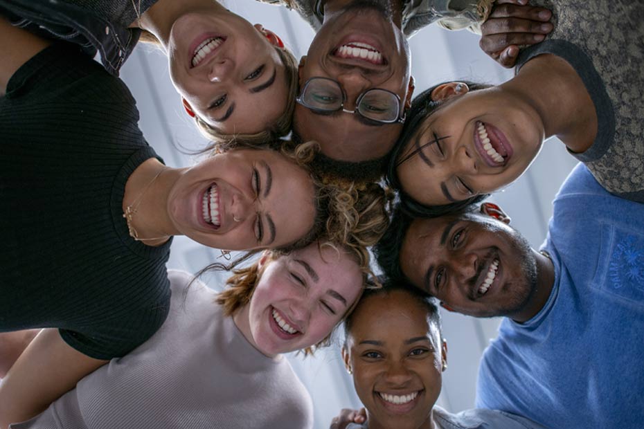 A group of multicultural international students in Canada with their heads together in a circle, looking down from above.