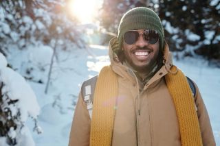 A smiling male international student wearing a warm coat and sunglasses, enjoying his first Canadian winter.