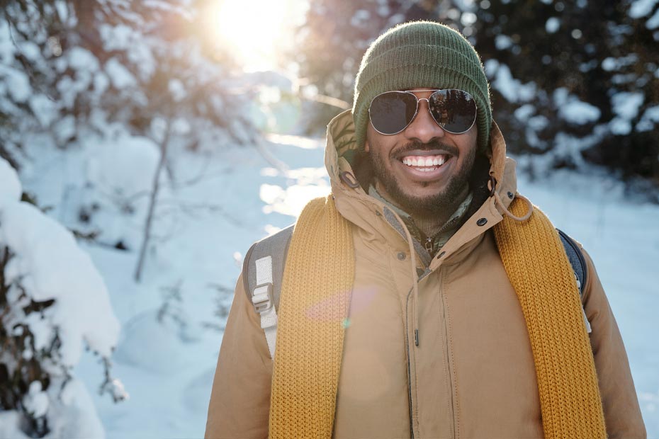 A smiling male international student wearing a warm coat and sunglasses, enjoying his first Canadian winter.