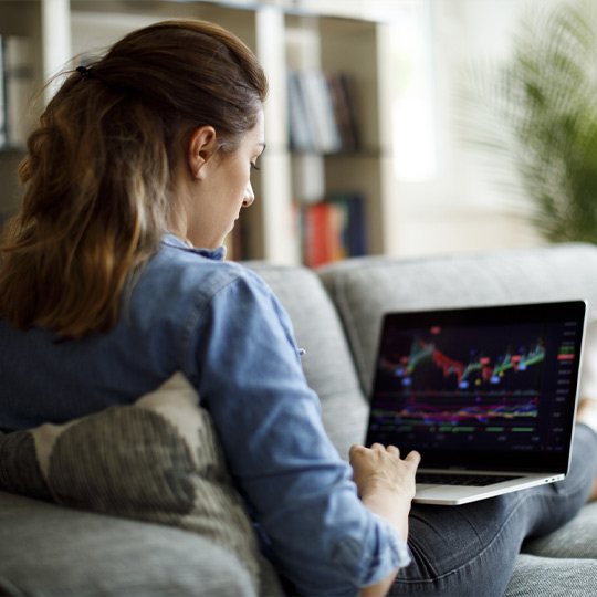 Girl on sofa looks at stock portfolio on laptop