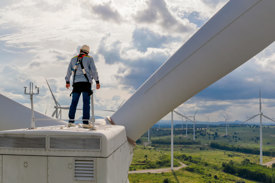 A wind turbine technician stands on top of a wind turbine