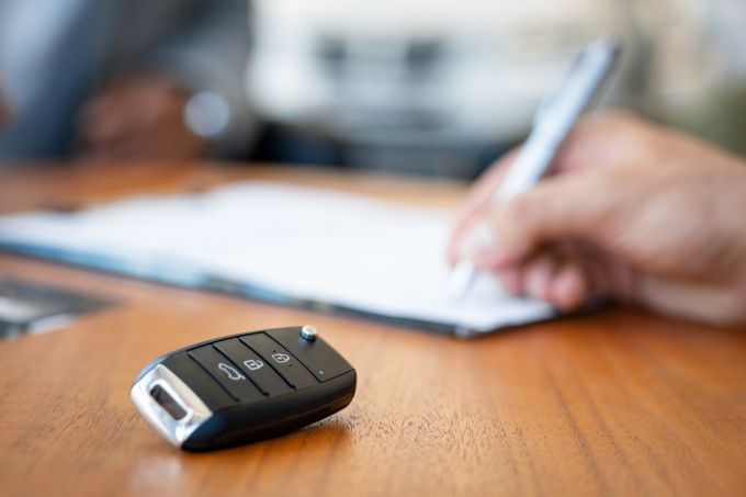 Visible hand at a desk signing an agreement with car keys in the foreground