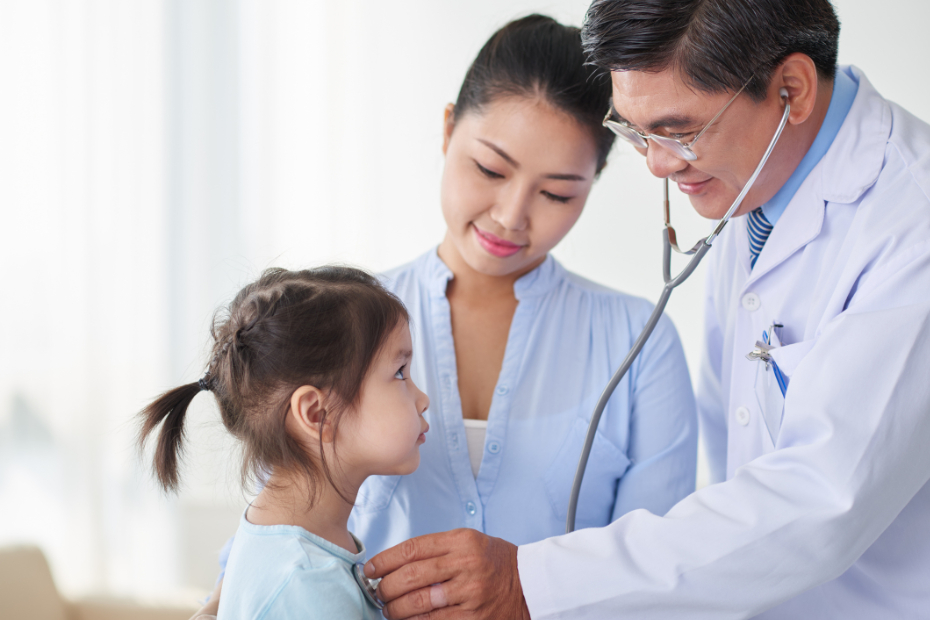 Young Asian girl and her mom looking at pediatrician while he examines her
