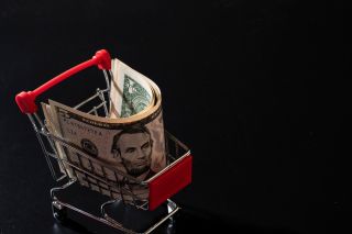 Miniature shopping cart on a black background filled with US dollars