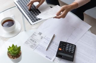 Top down view of a woman at a desk covered with bills and a calculator