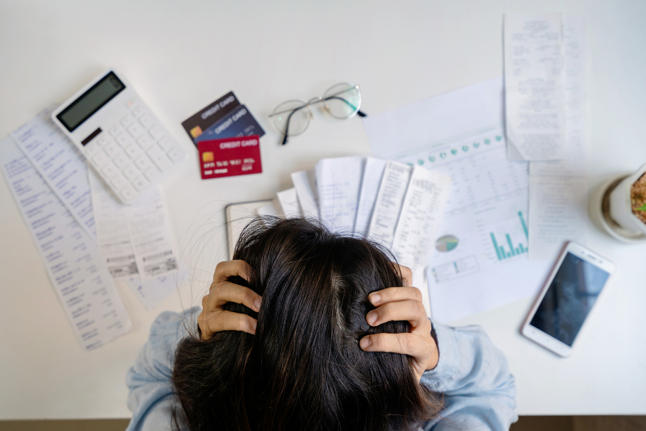 Stressed young woman surrounded by bills, calculating monthly expenses