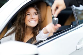 Smiling young brunette woman receiving the keys to her new car