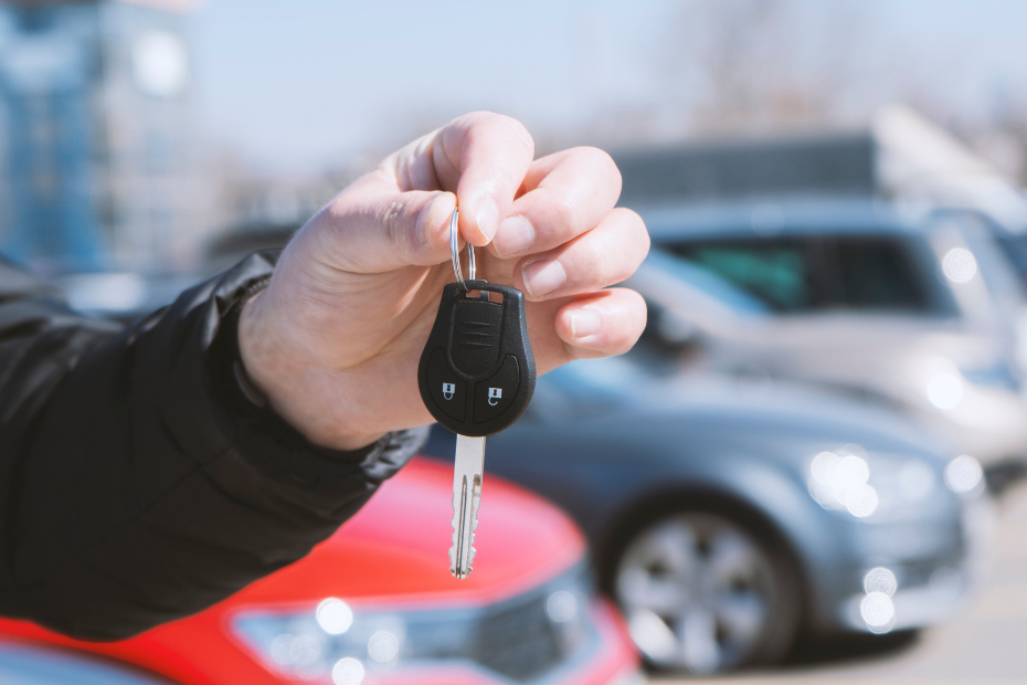 Out of focus car lot with a male hand holding a car key in the foreground