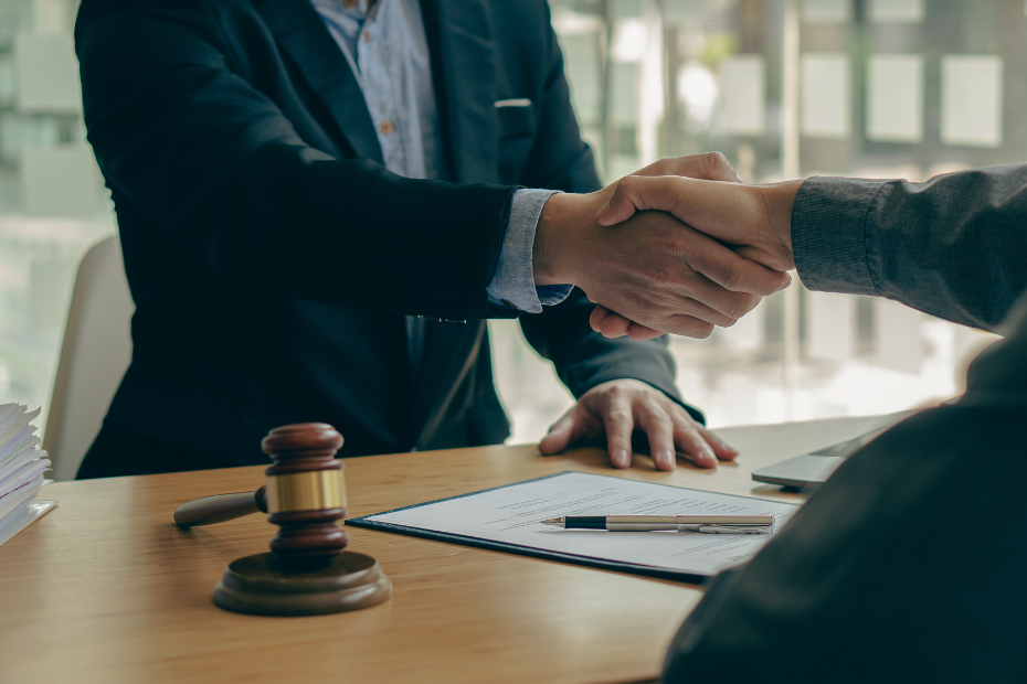 Two male hands shaking over paperwork and a gavel on a desk