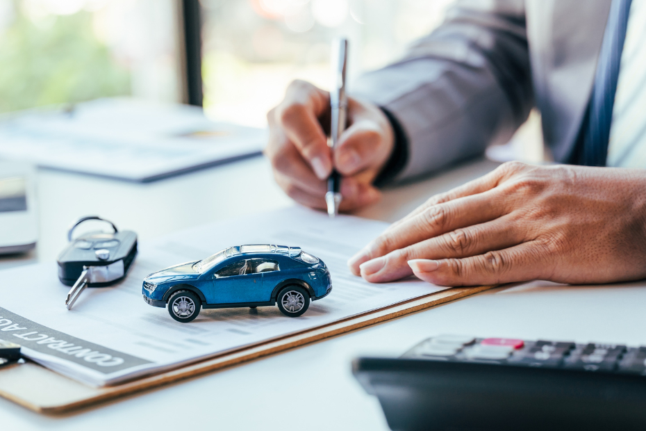 Man signing car loan paperwork with calculator beside him on a desk