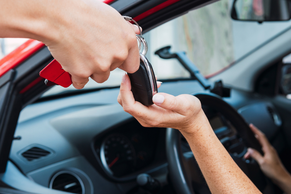 Car salesman handing keys to person in a red vehicle.