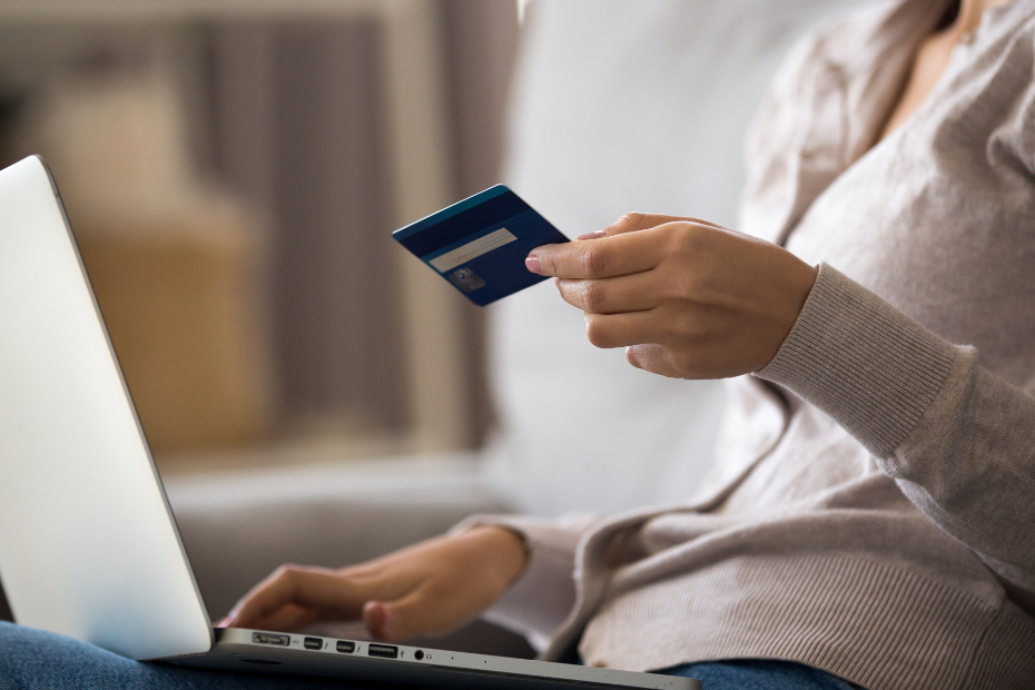 Out of focus woman using her laptop for online banking, holding a debit card