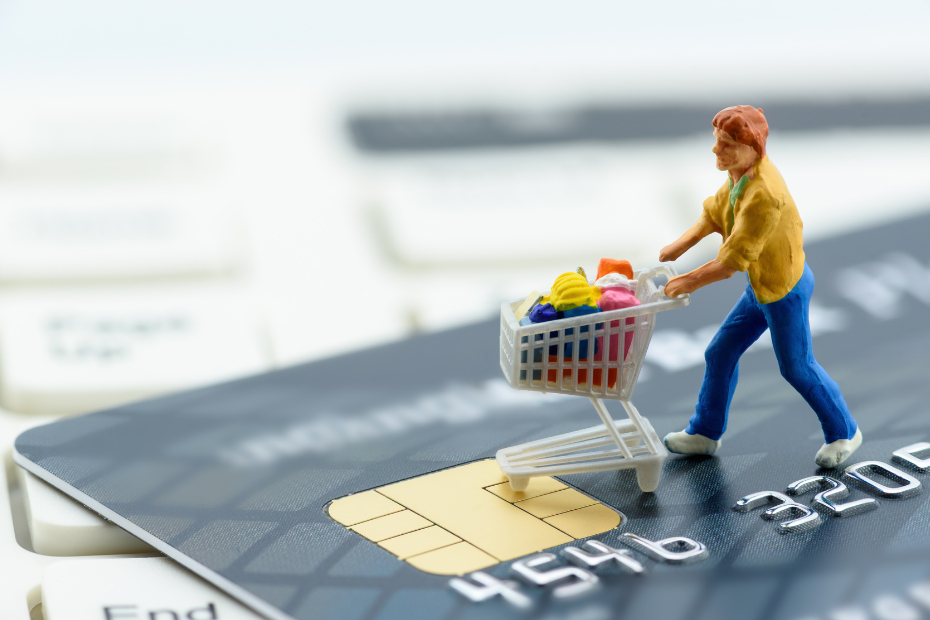 Miniature figurine shopper pushing a shopping cart on a smart credit card and a keyboard.