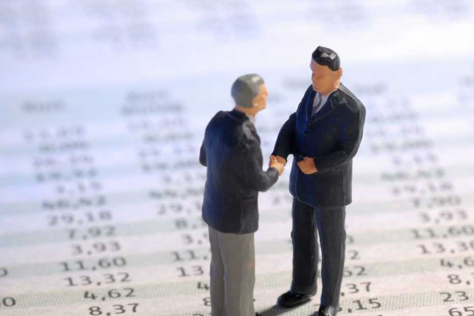 Two grey-haired miniature model figures standing on life-sized spreadsheets