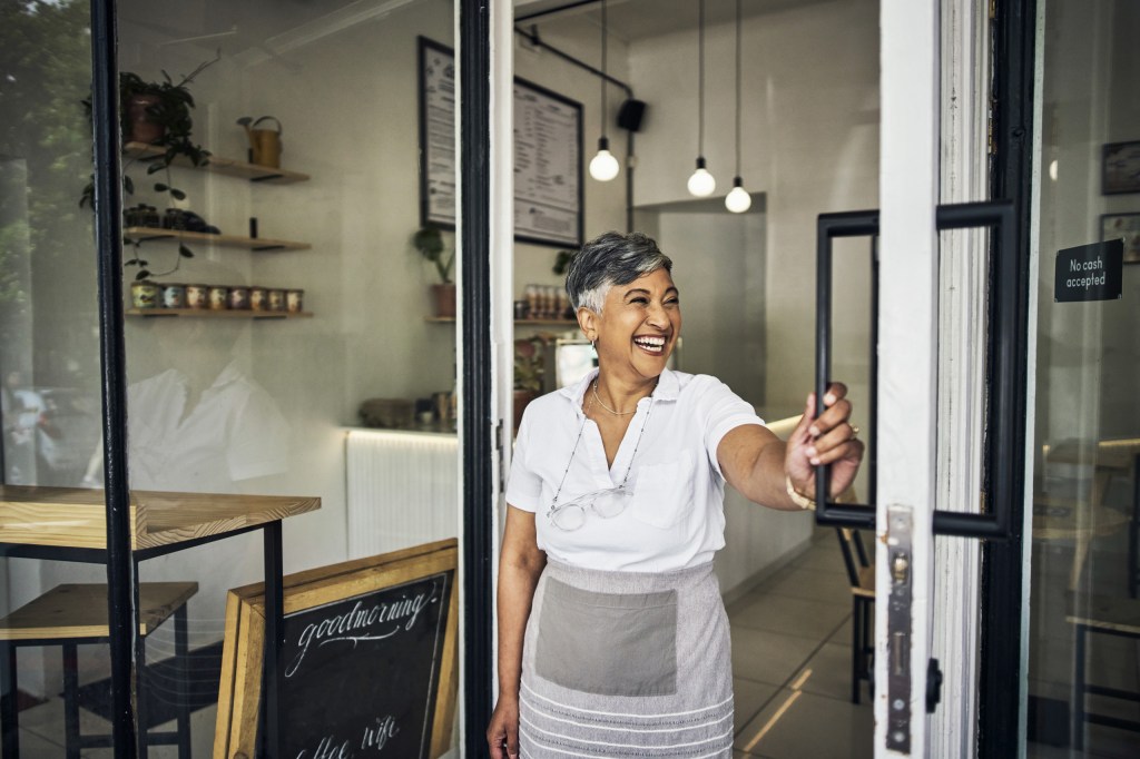 A retail owner smiling while opening the door of her shop. 