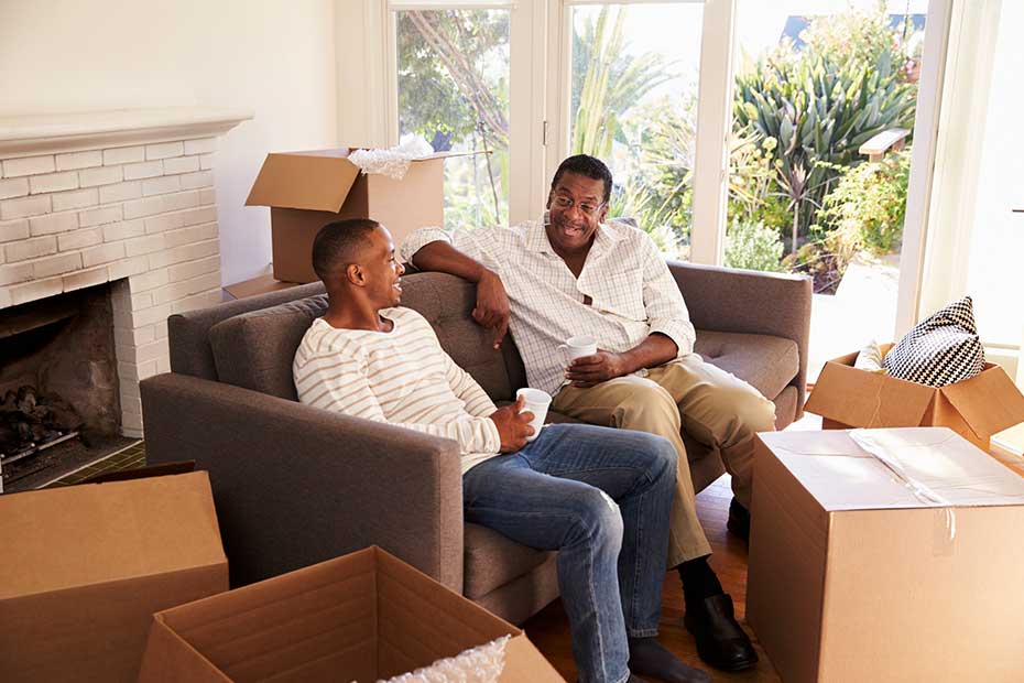 Father with young adult son sitting together in a living room, smiling and laughing conveying a sense of togetherness and harmony