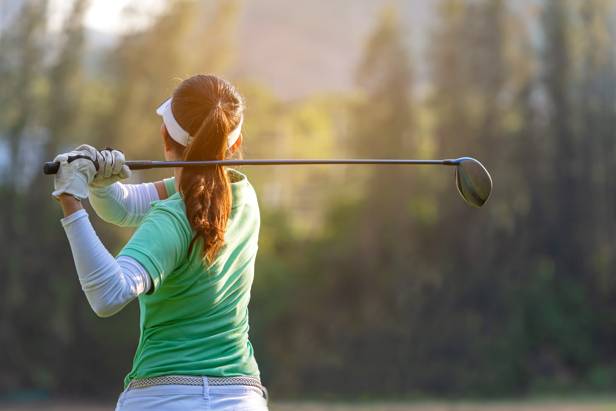 Asian sporty woman golf player doing golf swing tee off on the green sunset evening time, she presumably does exercise.