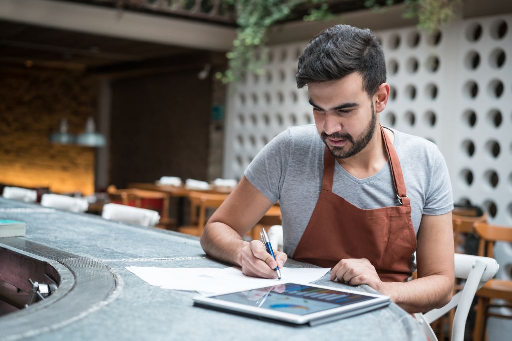 Young Latin American business man doing the books at a restaurant - entrepreneurship concepts