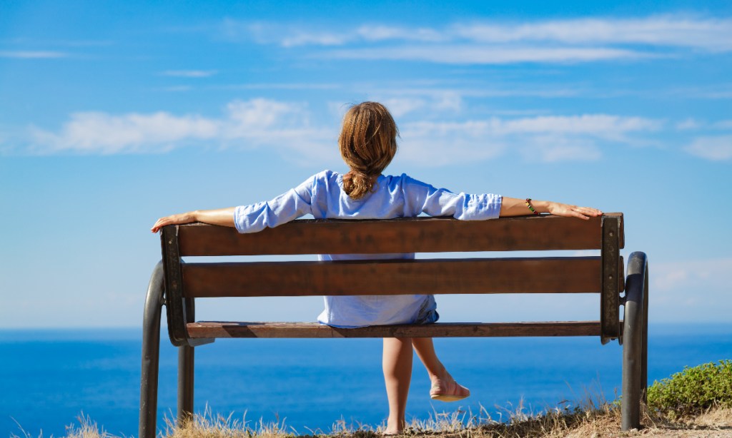 A girl sitting on a bench and overlooking waterbody.