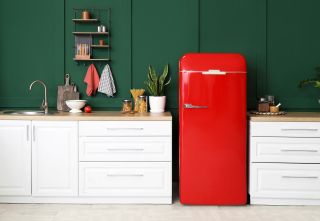 A modern, clean kitchen with a red refrigerator against a dark green wall