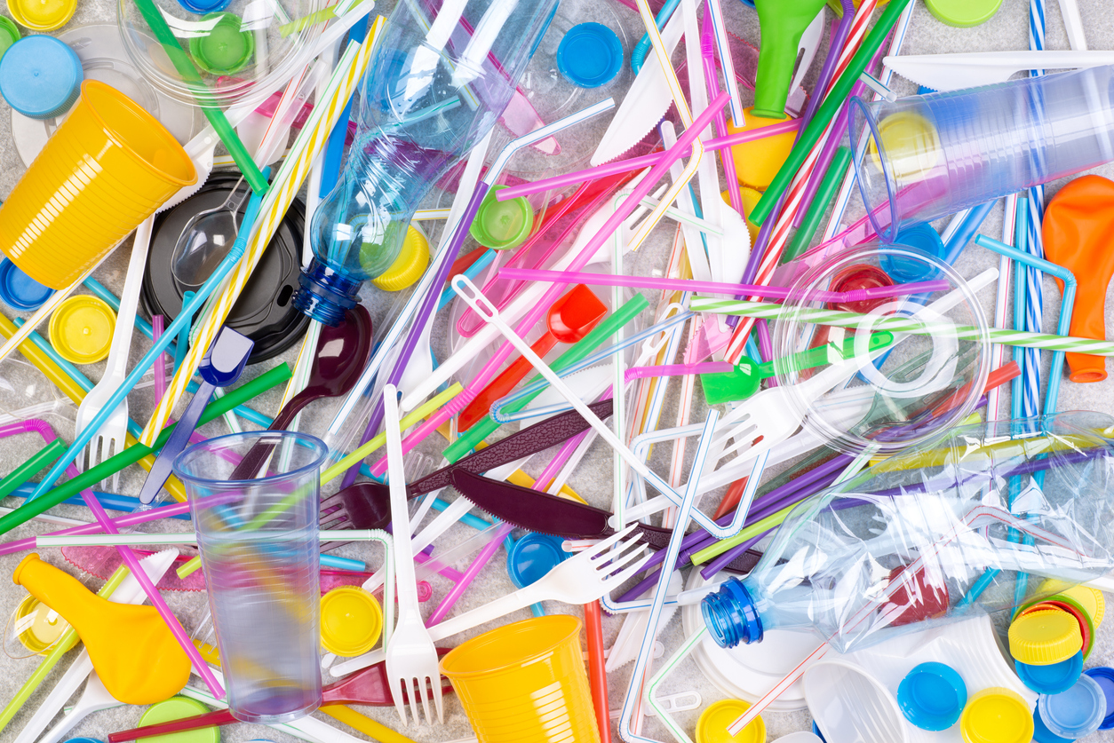Colourful plastic utensils, cups and bottles in a large pile.
