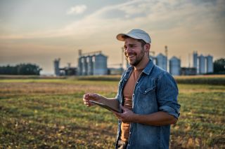 A farmer holding an ipad in the field, smiling.