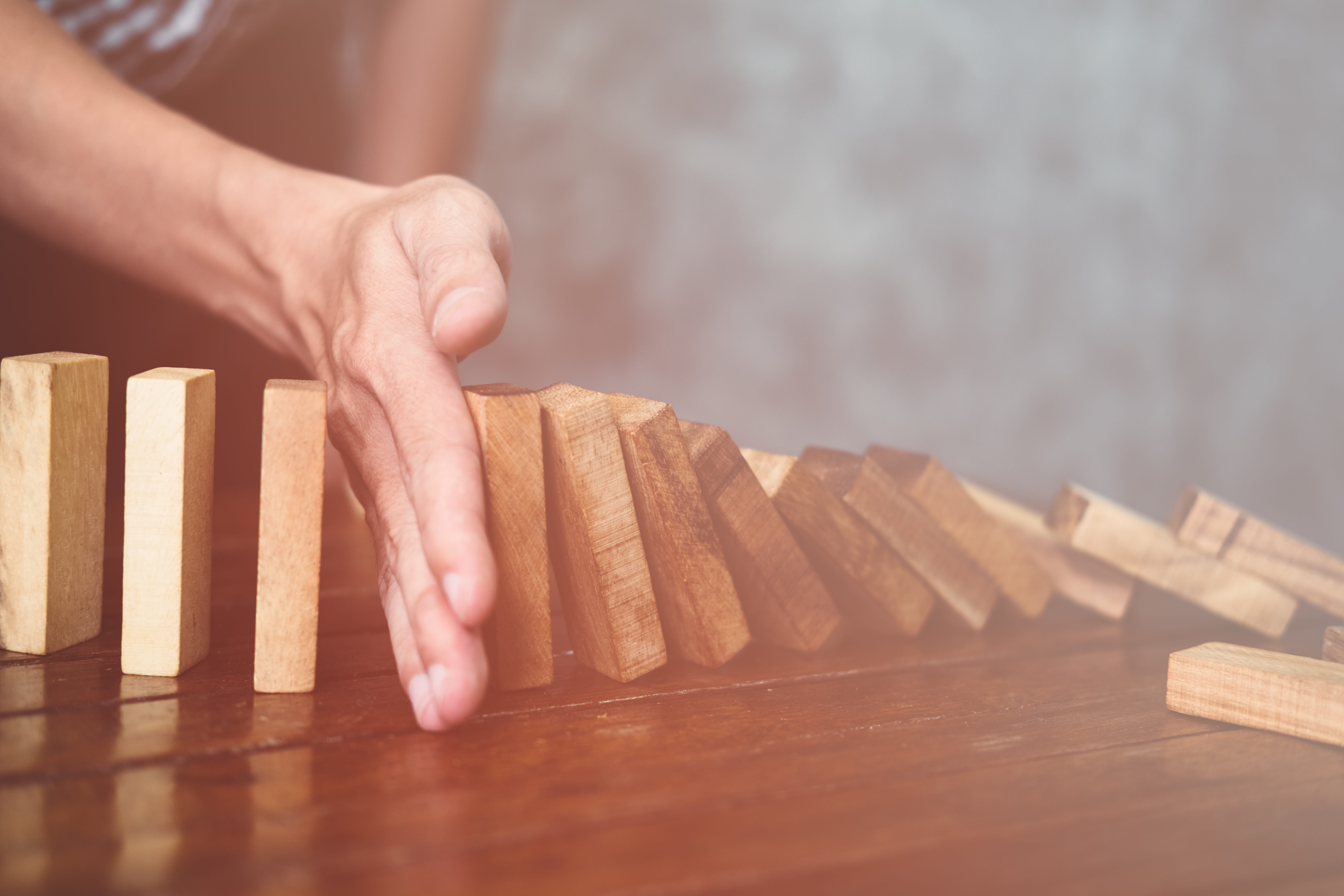 A hand pushing a row of dominoes over