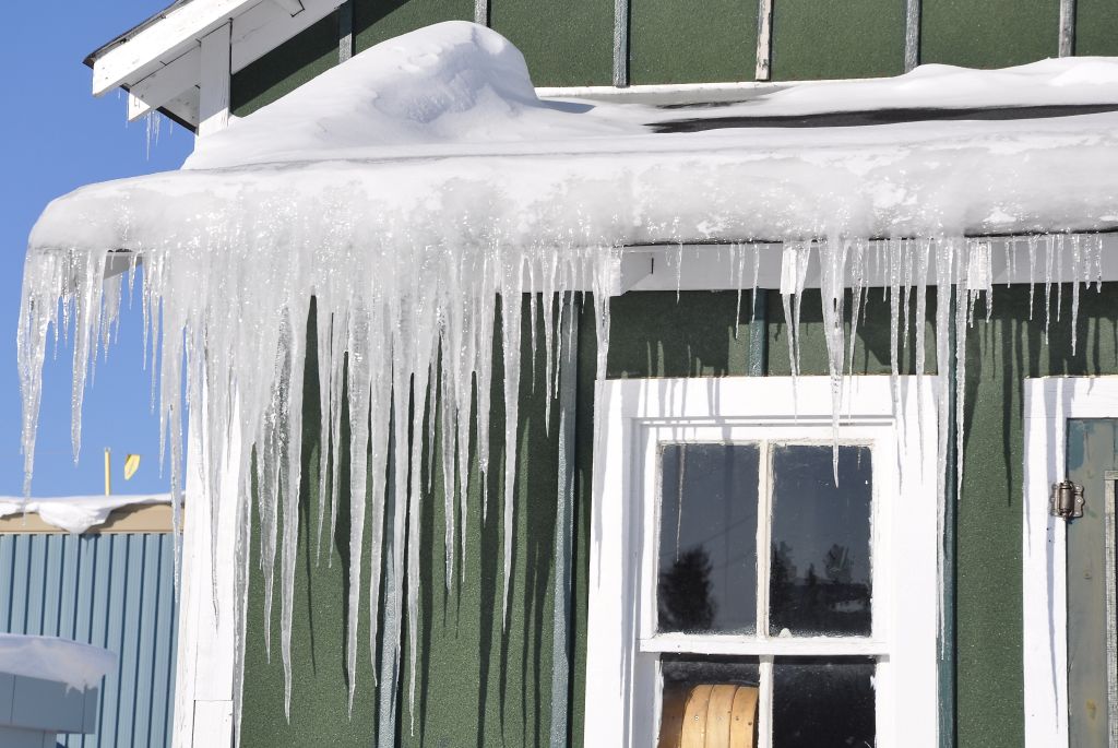Long icicles hang from the roof of a painted green house