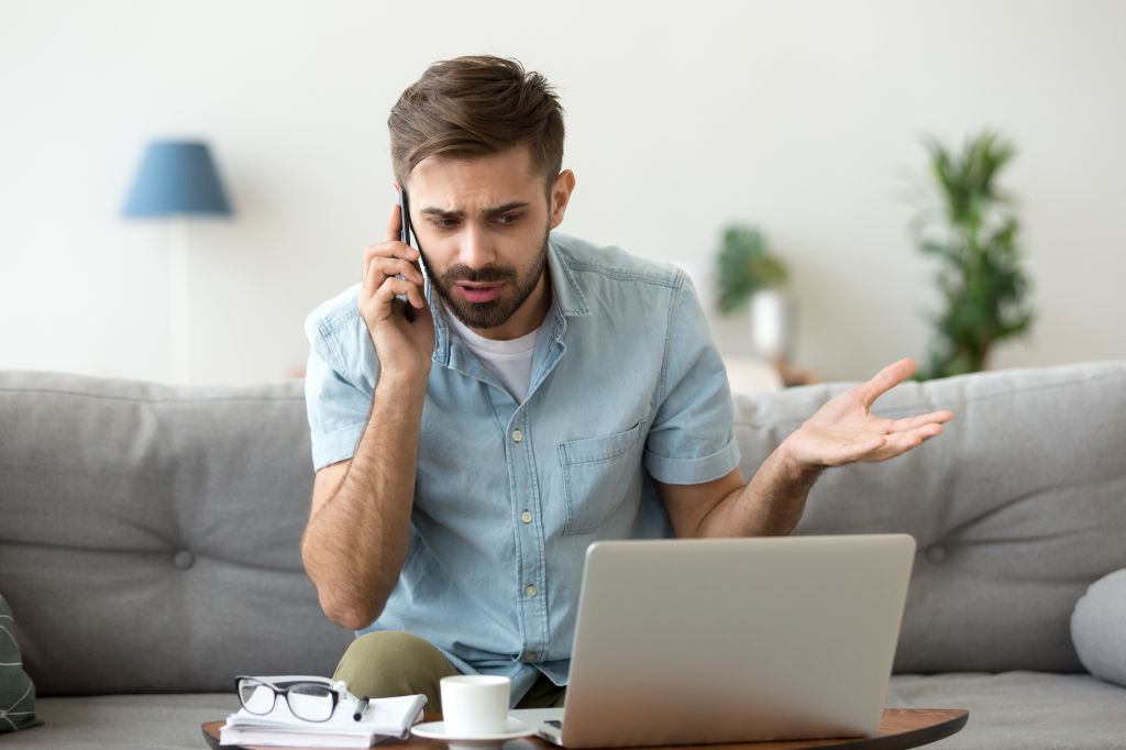 Angry man talking on phone disputing over computer laptop problem, stressed unsatisfied impatient customer arguing by mobile solving online difficulty with technical support complain on bad service