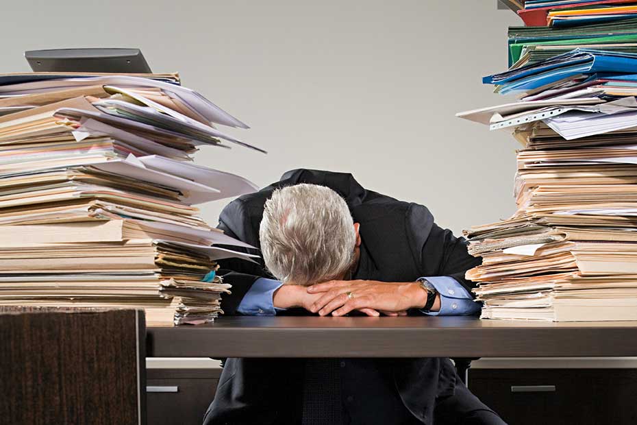 A stressed man behind a books with stacked books.