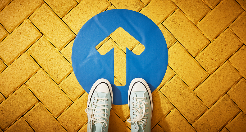 A pair of shoes on a yellow road behind an arrow pointing forward