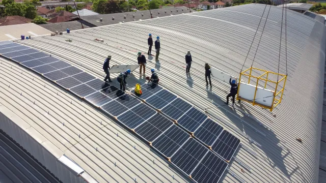 Workers install solar panels on the roof of a factory