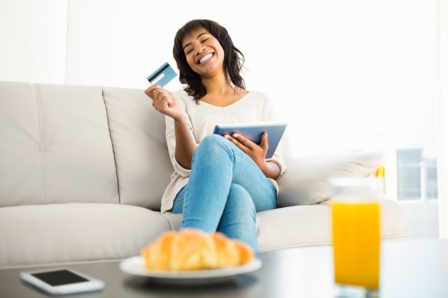 a girl sitting on couch with a bank card and tablet on hand