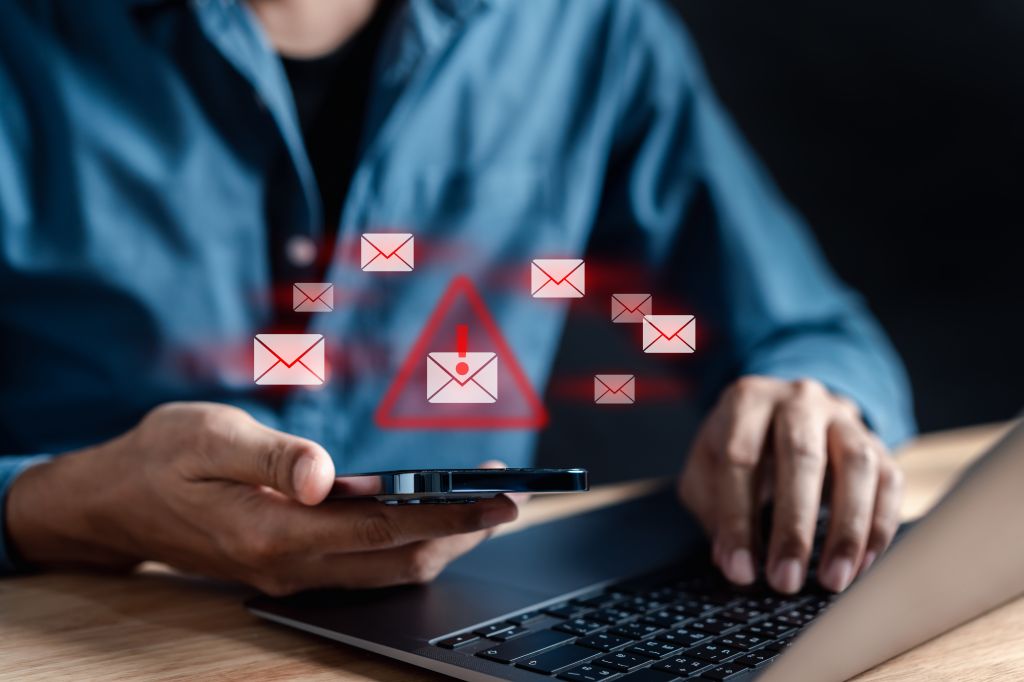 A businessman is on his laptop and mobile device. Email fraud alert graphics are overlayed onto the image.